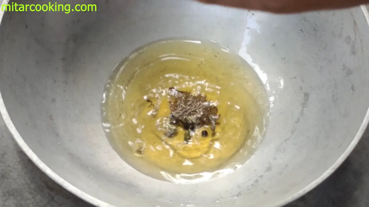 Adding the whole spices such as cumin seeds, cardamom, black pepper to the oil-ghee mixture
