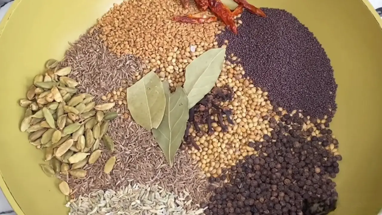 Adding coriander seeds, mustard seeds, cumin seeds, fenugreek seeds, green cardamom pods, black peppercorn, bay leaves, fennel seeds, chili pepper, cloves.