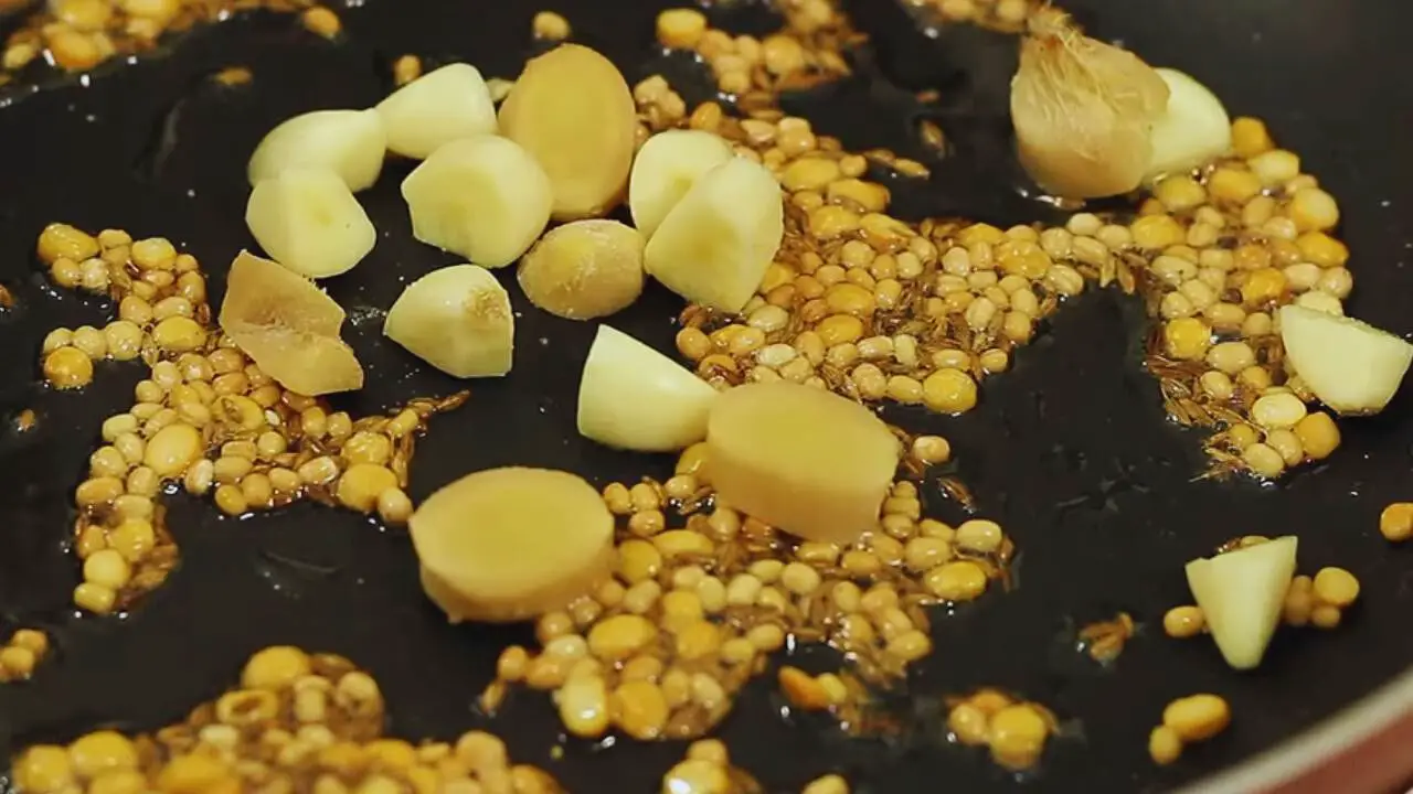 Adding 1 small piece of ginger of about 1 inch size, deskinned and chopped roughly, and 3 cloves of garlic, also deskinned and chopped roughly, to the ingredients in the frying pan