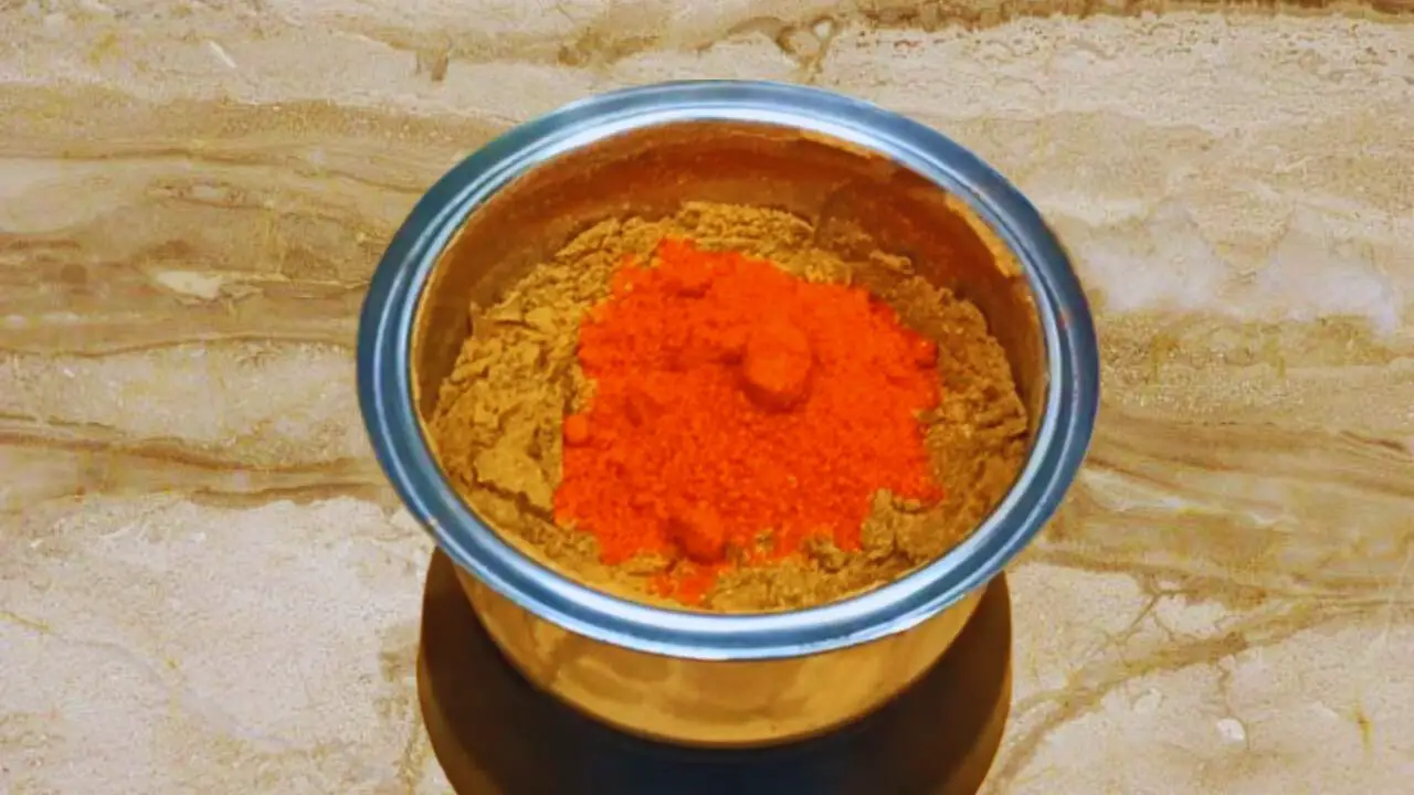 Adding some powdered ingredients to the ground spices in the grinder