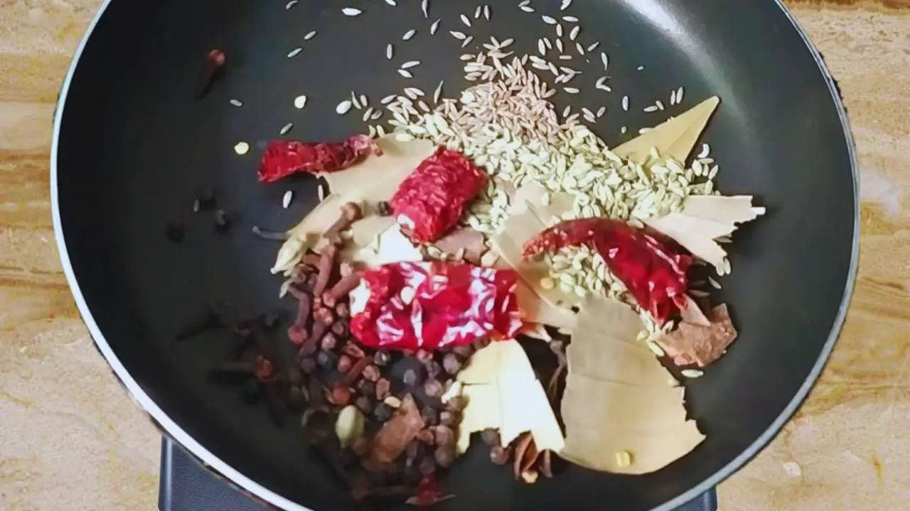 Putting 1 tsp of black peppercorns, 1 tsp of cloves, 4 small pods of green cardamom, 1 tsp of small cinnamon sticks, 2 pieces of bay leaves, 3 pieces of star anise, 2 medium pieces of dry red chilies, 1 tsp cumin seeds, and 1 tsp of fennel seeds in heated pan