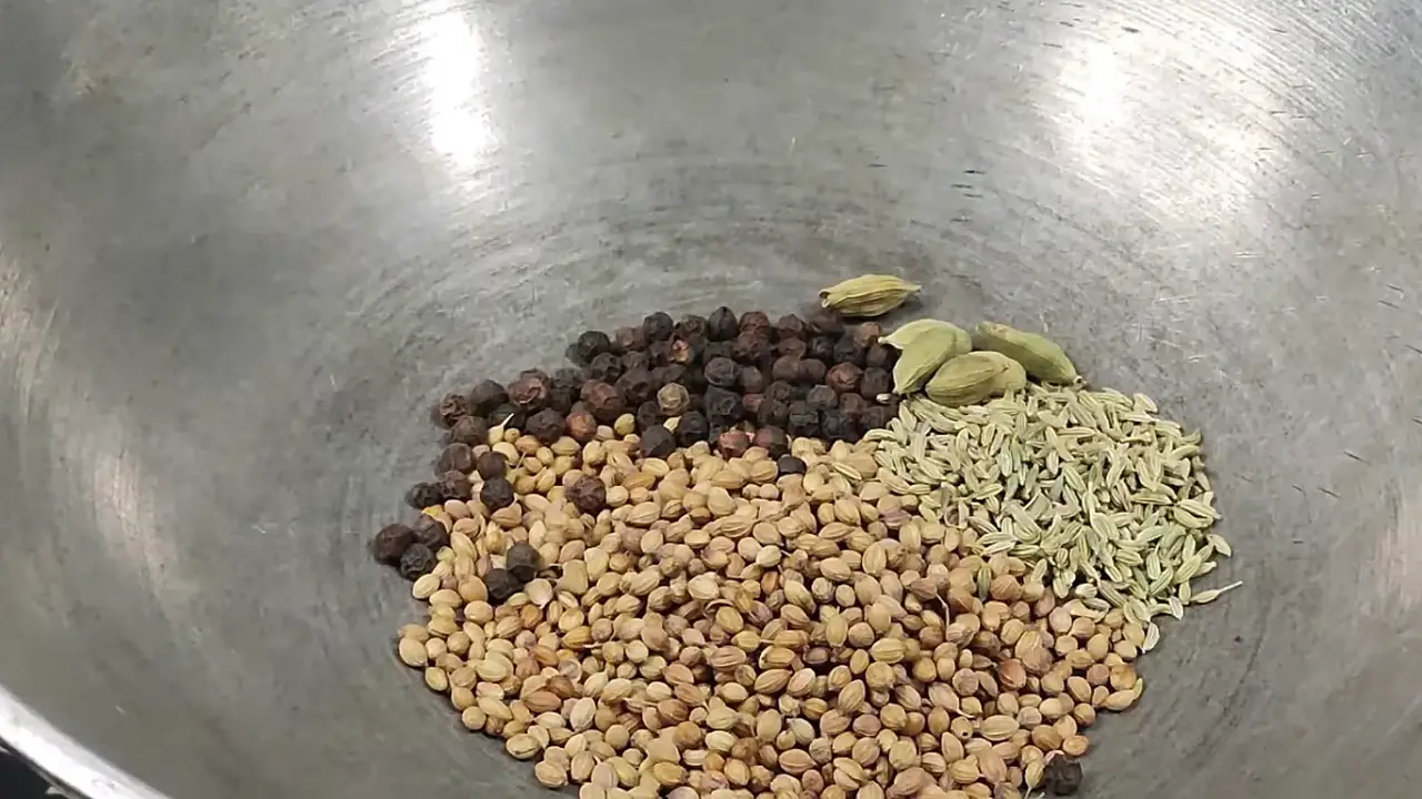 Putting 5 tsp of coriander seeds, 1 tsp of black pepper, 1 tsp of fennel seeds, and 5 pods of green cardamom in the hot wok