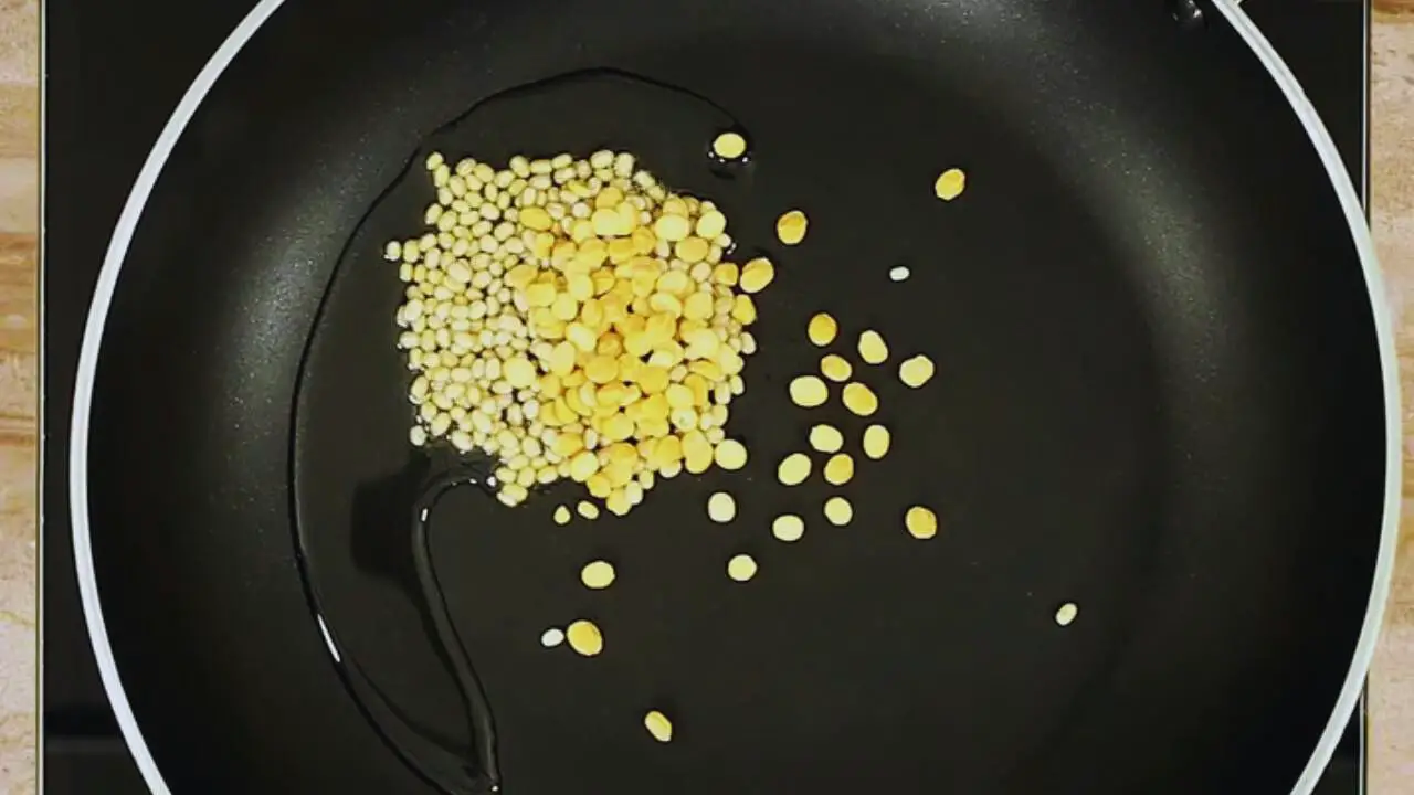 Putting 1.5 tsp of split black lentils (urad dal) and 1 tsp of chickpea lentils (chana dal) in the pan