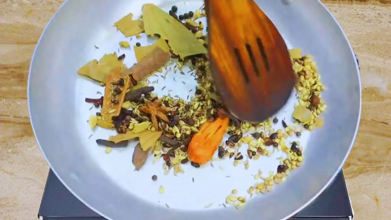 Putting all the whole spices such as 1 tbsp of white cumin seeds, ½ tbsp of black cumin seeds, ½ tbsp of black pepper, 1 tbsp of fennel seeds, 1 tbsp of coriander seeds, ½ piece of nutmeg, ½ piece of mace, 3 cinnamon sticks of 1-inch size, ½ tsp of tailed pepper or cubebe, ½ tsp of green cardamom, 1 tsp of cloves, 5 pieces of long pepper (pippali) of about 1-inch size, 1 tbsp dry pomegranate seeds, 4 pieces of black cardamom, 4 pieces of star anise, and 3 pieces of bay leaves (torn) in frying pan