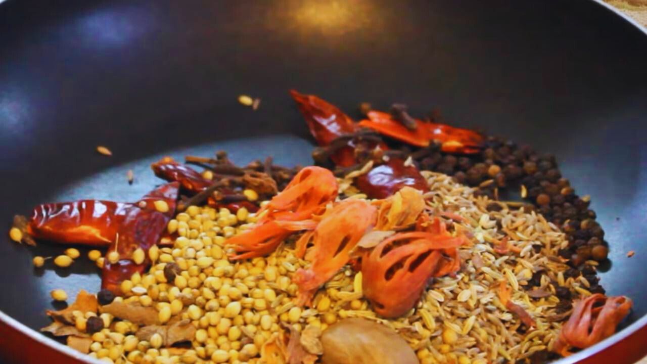 Putting 7 medium pieces of dry Kashmiri red chilies, one nutmeg, 1 tsp cinnamon sticks broken into small pieces, ½ tsp cloves, 1 tsp of black pepper, 3 tsp of coriander seeds, 2 tsp of cumin seeds, 1 tsp of fennel seeds, and one large mace torn into pieces into cooking pan