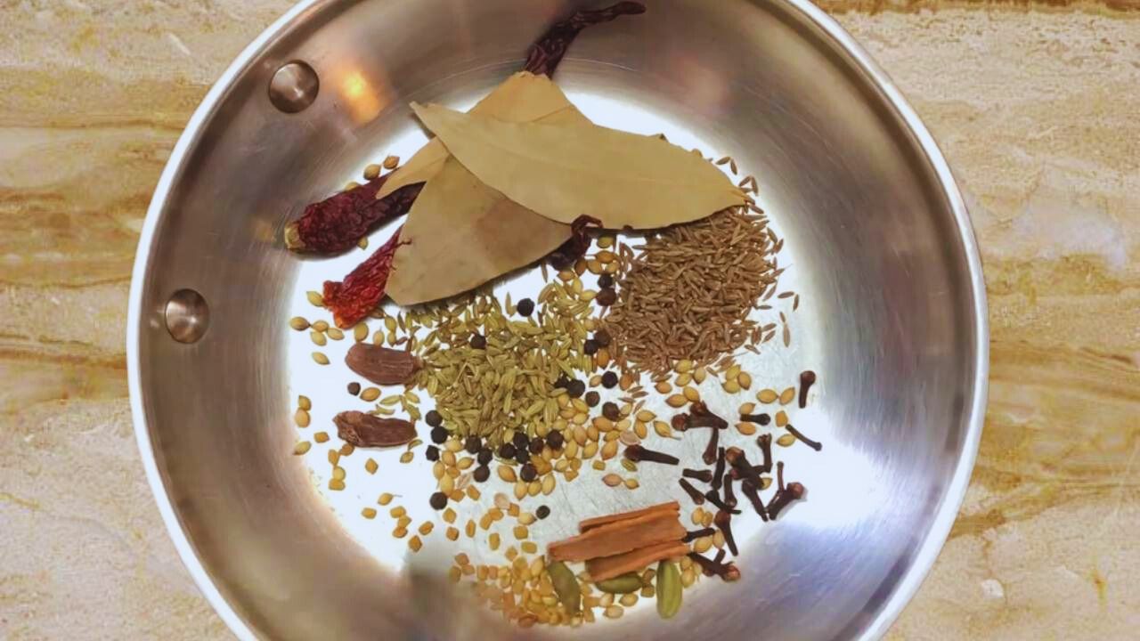 Putting 1 tsp of coriander seeds, 1 tsp of cumin seeds, 2 pieces of dry red chilies, 2 pieces of black cardamom pods, 3 pieces of green cardamom pods, ¼ tsp of fenugreek seeds, ¼ tsp of black pepper, ¼ tsp of cloves, 1 tsp of fennel seeds, 3 cinnamon sticks of 1-inch size, and 3 pieces of bay leaves of medium size in a pan