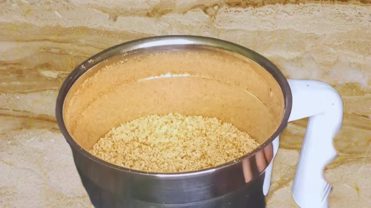 Adding the roasted sesame seeds to the ground spices in the grinder