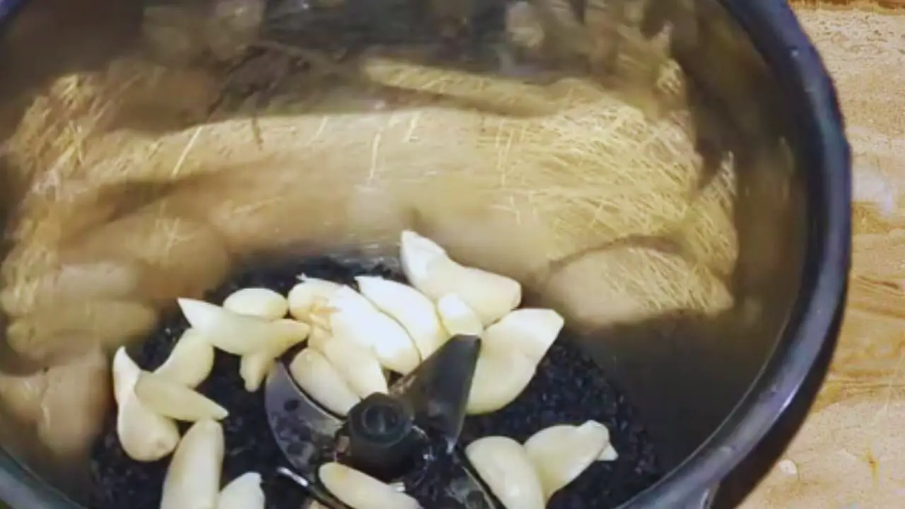 Adding 15 to 20 medium-sized cloves of fresh garlic into the grinder