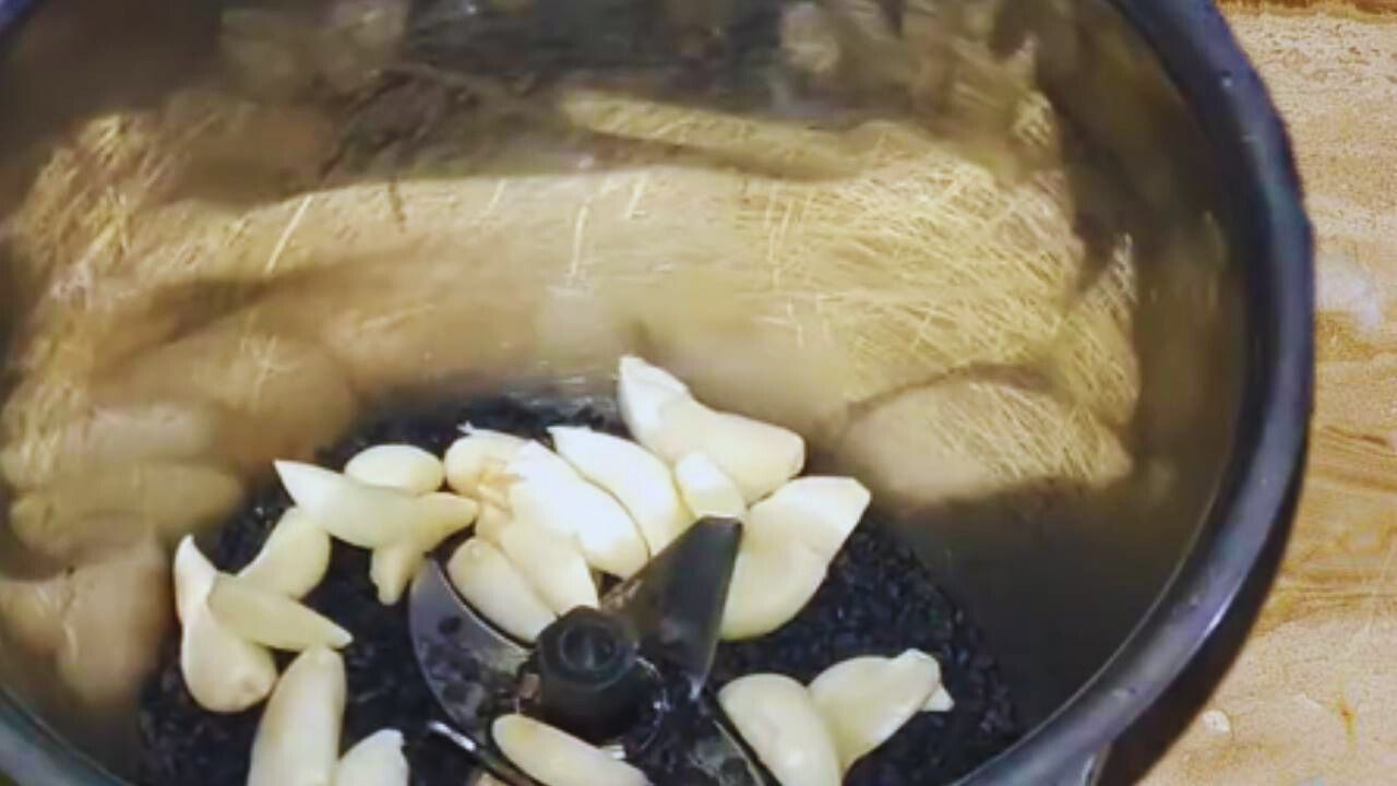 Adding 15 to 20 medium-sized cloves of fresh garlic into the grinder