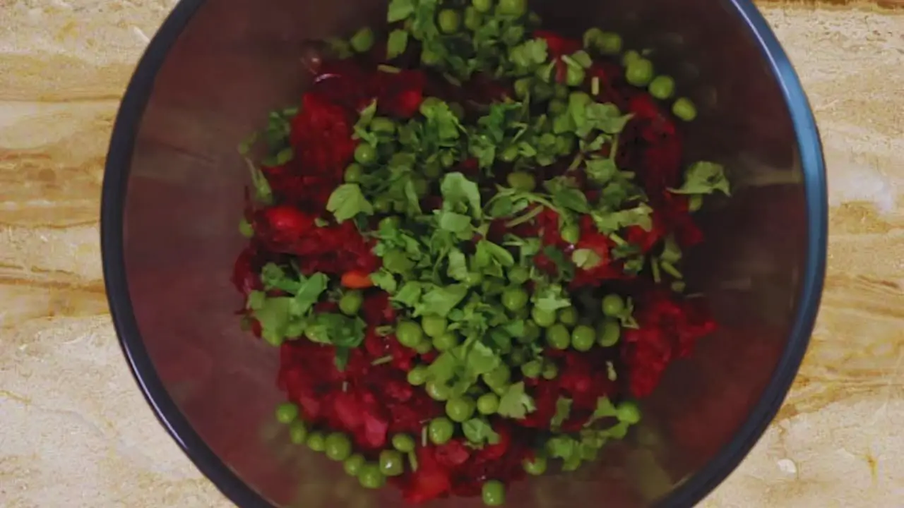Adding green peas and coriander leaves to the beetroot cutlet mixture 