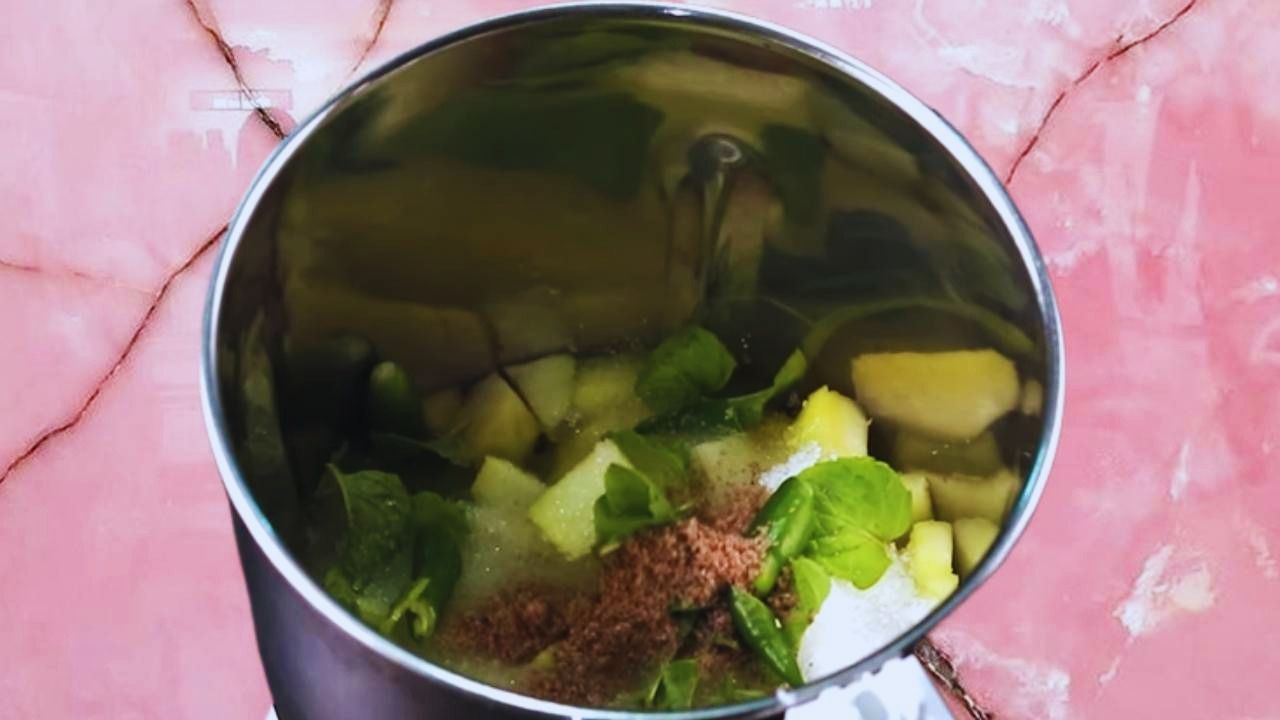 Raw mango juice recipe step 2 Adding mint leaves, black salt and chilies to mango pieces in the mixie jar